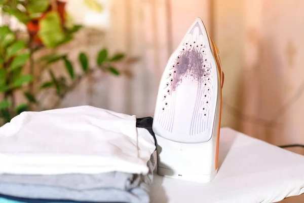 Una pila de camisetas y una plancha quemada en una tabla de planchar. Funciones domésticas. - foto de stock