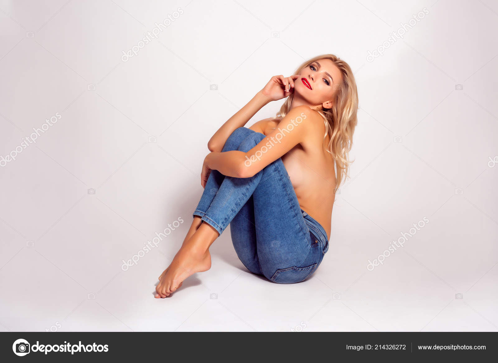 Татуированная блондинка в джинсах и с голой грудью стоит у стены