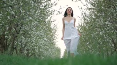 bahar moda portre uzun kahverengi saçlı beyaz elbiseli güzel bir mutlu genç kadının çalıştırın ve çiçek açması Bahçe keyfini