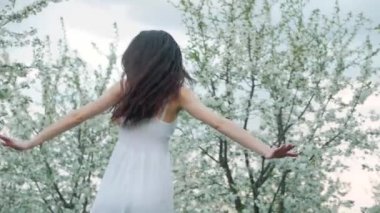 bahar moda portre uzun kahverengi saçlı beyaz elbiseli güzel bir mutlu genç kadının çalıştırın ve çiçek açması Bahçe keyfini