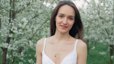 bahar moda portre uzun kahverengi saçlı beyaz elbiseli güzel bir mutlu genç kadının çalıştırmak ve çiçek açması bahçede çiçek kokusu tadını çıkarın