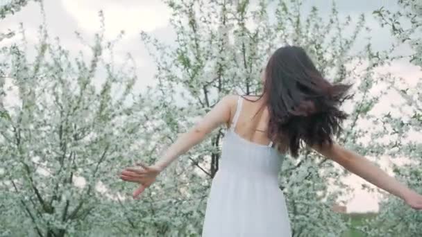 Retrato de moda de primavera de una hermosa mujer joven feliz en vestido blanco con pelo largo y marrón correr y disfrutar del jardín en flor — Vídeos de Stock