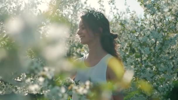 Giovane ragazza vicino a un bellissimo albero fiorito. Giardino fiorito in primavera. Bella ragazza che tiene un ramo e fiori nelle sue mani — Video Stock