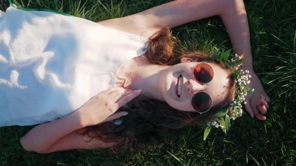 Slow Motion: Bovenaanzicht shot van een Kaukasische meisje in een witte bloemen jurk liggend in het gras — Stockvideo