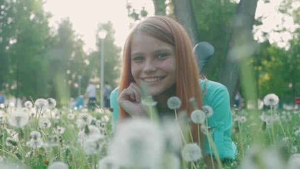 Mooie jonge vrouw met rood haar liggend op het veld in het groene gras en paardenbloem. Buitenshuis. Geniet van de natuur. Gezonde glimlachend meisje op voorjaar gazon. Allergie vrije concept — Stockvideo