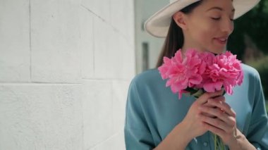 Mutlu şık sevimli genç karışık ırk kadın moda Blogger mavi yazlık elbise ve beyaz şapka yaz sokakta poz portresi, whith pembe çiçekler güneş parlıyor