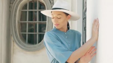 Mutlu şık sevimli genç karışık ırk kadın moda Blogger mavi yazlık elbise ve beyaz şapka yaz sokakta poz portresi, Güneş parlıyor