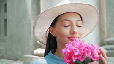Mutlu şık sevimli genç karışık ırk kadın moda Blogger mavi yazlık elbise ve beyaz şapka yaz sokakta poz portresi, whith pembe çiçekler güneş parlıyor