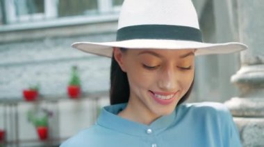 Mutlu şık sevimli genç karışık ırk kadın moda Blogger mavi yazlık elbise ve beyaz şapka yaz sokakta poz portresi, Güneş parlıyor