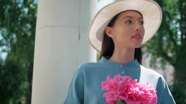 Happy Stylish Charming jeune femme métissée Fashion Blogger Marcher le long de la rue urbaine européenne en robe d'été bleue et chapeau blanc et profiter de vacances voyage aventure vacances fleurs blanches rose — Video