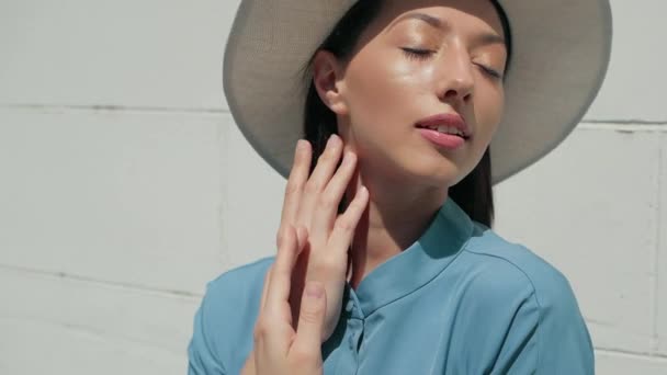 Retrato de feliz elegante encantadora joven mujer de raza mixta Blogger de moda en vestido azul de verano y sombrero blanco posando en la calle de verano, el sol está brillando — Vídeos de Stock