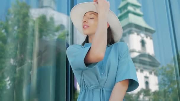 Портрет счастливой стильной очаровательной молодой смешанной расы женщина Блогер моды в синем летнем платье и белая шляпа позирует на летней улице, солнце светит — стоковое видео
