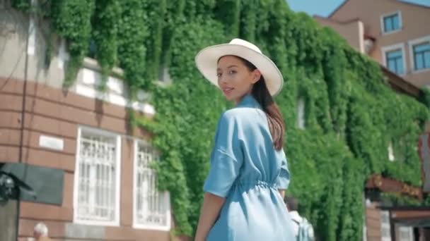 Happy Stylish Charming jeune femme métissée Fashion Blogger Marcher le long de la rue urbaine européenne en robe d'été bleue et chapeau blanc et profiter vacances voyage aventure — Video