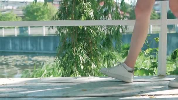 Flickor fötterna i vita sneakers är på vita brädor mot bakgrund av en grön willow blad — Stockvideo