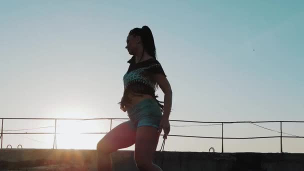 Donna danzante. silhouette felice corsa mista donna danza prestazioni con lunghi dreadlocks in pantaloncini su sfondo tramonto — Video Stock