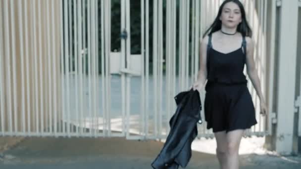 Прогулянка прохолодною модою серйозна жінка-підліток в чорній, шкіряній куртці, кольє курка з довгим темним волоссям і помадою — стокове відео