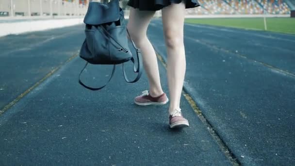 Ragazza cammina in possesso di uno zaino di pelle nera. concentrarsi sui suoi piedi in scarpe da ginnastica rosse — Video Stock