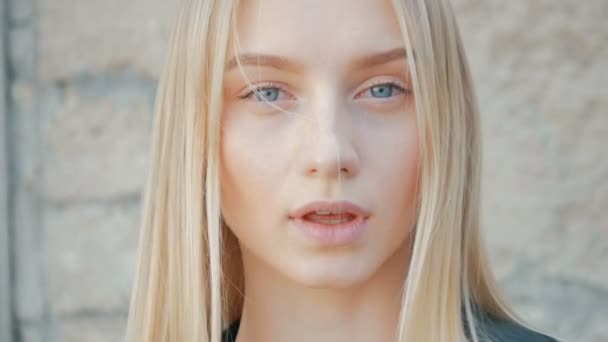 Portrait de mode d'une belle jeune femme aux yeux bleus et aux cheveux blonds dans une veste en cuir à l'extérieur — Video