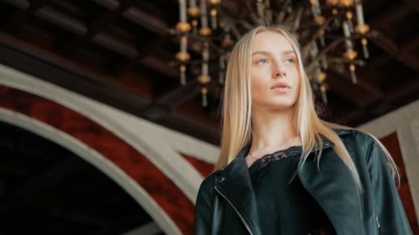 Portrait de mode d'une belle jeune femme aux yeux bleus et aux cheveux blonds dans une veste en cuir intérieure — Video