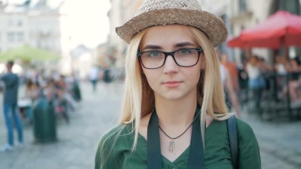 Portret van een mooi blond meisje met bril, een hoed en een blauwe jeans-jasje. — Stockvideo