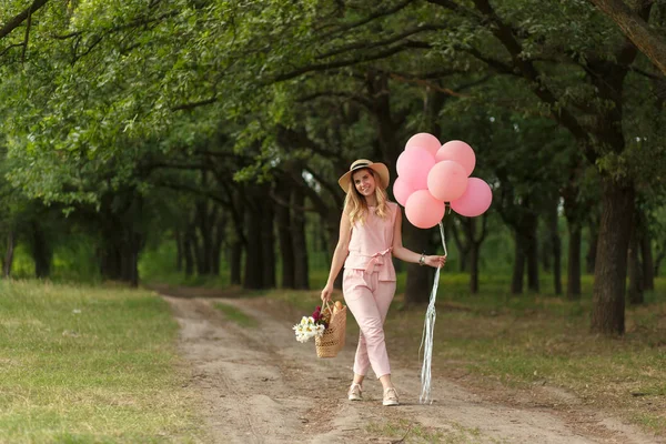 枝編み細工品バスケット ピンクの風船 花の国の道路の上を歩く女性 — ストック写真
