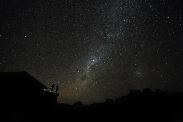 Couple on rooftop watching mliky way and stars in the night sky on Bali island.