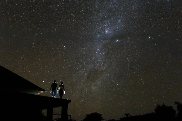 Couple on rooftop watching mliky way and stars in the night sky on Bali island.