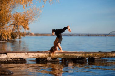Genç kadın şehir arka plan ile sessiz ahşap iskelede Yoga egzersiz pratik. Spor ve eğlence şehir acele.