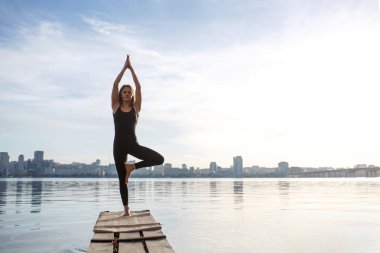 Genç kadın şehir arka plan ile sessiz ahşap iskelede Yoga egzersiz pratik. Spor ve eğlence şehir acele.