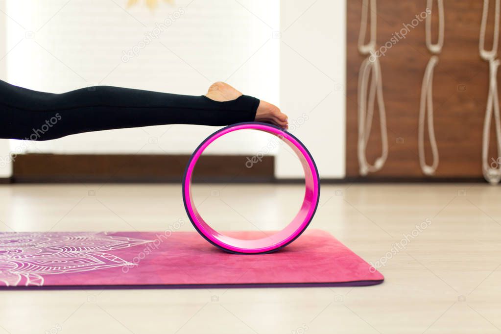 young woman in a sportswear yoga exercises with a yoga wheel in the gym. Stretching and wellness lifestyle.