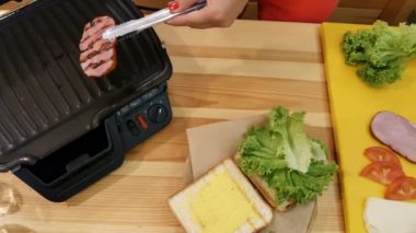 Bir sandviç mutfakta yemek. Üstten görünüm el maşa ile bir sıcak sadece tost parça ızgara et alır ve salata ile ekmek üzerine vardiya