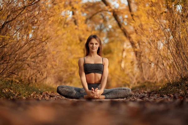 Young woman practicing yoga exercise in autumn park with yellow leaves. Sports and recreation lifestyle.