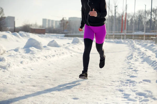 girl in sportswear run on a snow-covered stadium Fit and sport lifestyle. Run and listening music. Sport lifestyle.