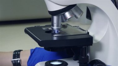 Öğrenci hekim mikroskopla kan analiz eder. Mikroskop yakın çekim kurulumu, araştırma malzemesi platformuyla mikroskop objektif uzak hareket gider