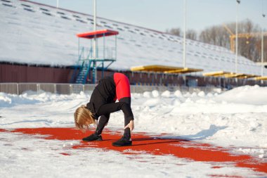 Kırmızı tozluk karlı bir stadyumda kırmızı bir koşu parkuru üzerinde egzersiz germe Genç beyaz kadın sarışın. uyum ve spor yaşam tarzı