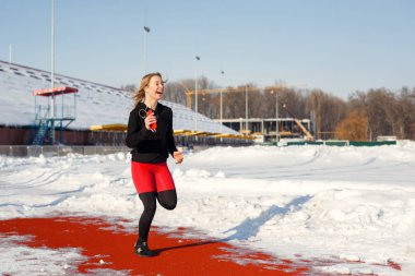 kız bir karla kaplı Stadyumu uyum ve spor yaşam tarzı üzerinde çalışan kırmızı rayına çalıştırmak spor giyim. Çalışma ve müzik dinleme. Spor yaşam tarzı.
