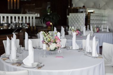 Beyaz peçeteler beyaz tabaklar ve restoranda sunulan Tablo ortasına taze çiçekler buket stand. temiz beyaz yemekleri düzeni üzerinde beyaz masa örtüsü