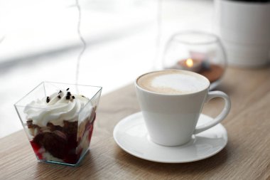 Beyaz fincan beyaz daire üzerinde sıcak cappuccino ve ahşap bar masa pencere yanında kırmızı kadife tatlı. Dışarıda soğuk karlı havalarda.