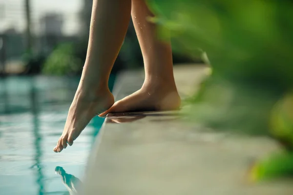 Primer plano joven pierna femenina toque agua azul en la piscina —  Fotos de Stock