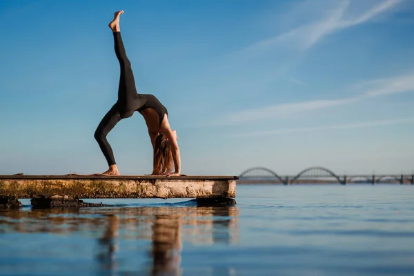 Young woman practicing yoga exercise at quiet wooden pier with c