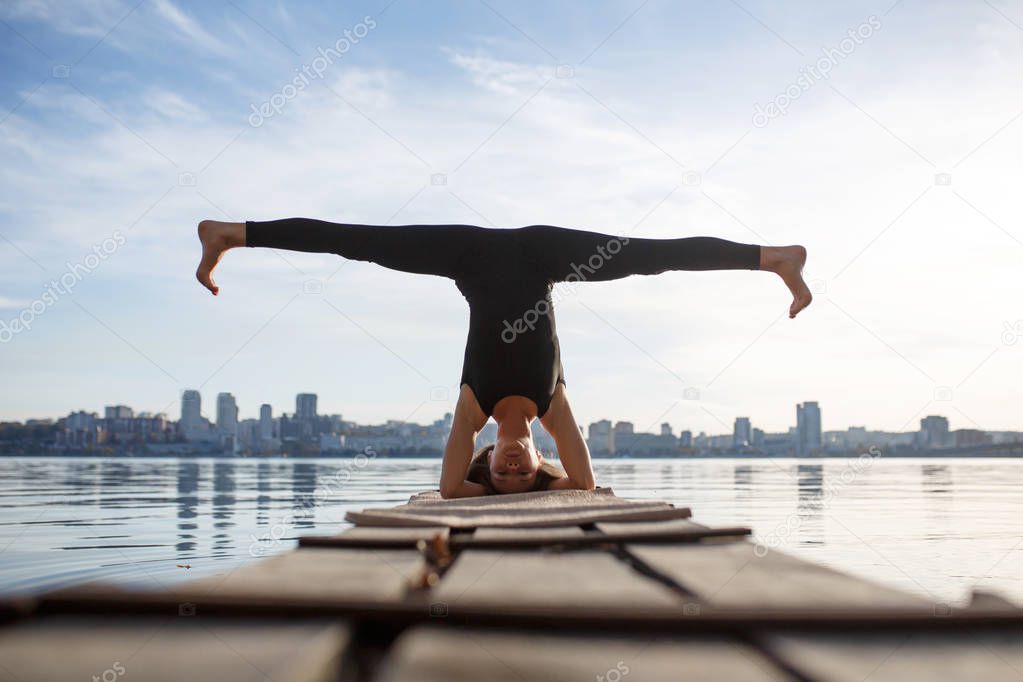 Young woman practicing yoga exercise at quiet wooden pier with c