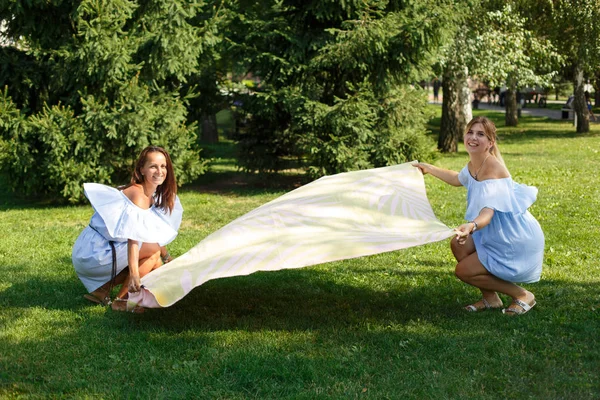 Dos chicas en un prado verde extendieron una manta de picnic. Fines de semana — Foto de Stock