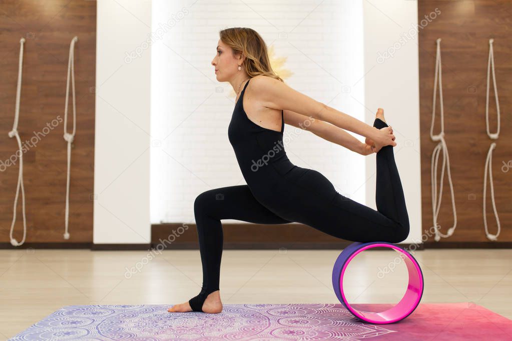 young woman in a sportswear yoga exercises with a yoga wheel in 