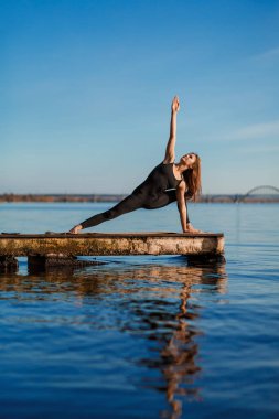 Genç kadın şehir arka plan ile sessiz ahşap iskelede Yoga egzersiz pratik. Spor ve eğlence şehir acele