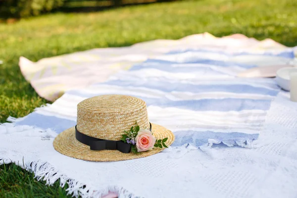 緑の芝生の明るい夏の日の背景に白のピクニック毛布の上に新鮮な花をあしらったストロー ハットが横たわっていた。夏の週末のレジャー — ストック写真