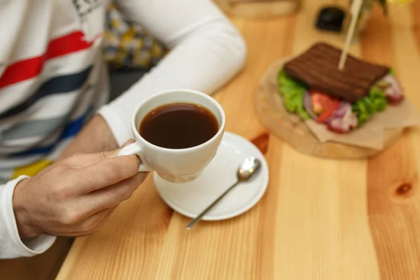 Man houdt witte kop koffie in de sandwich achtergrond — Stockfoto