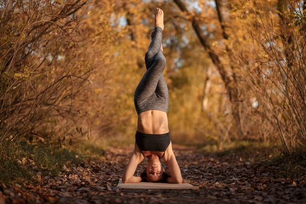 Молода жінка практикує вправи йоги в осінньому парку з жовтим — стокове фото