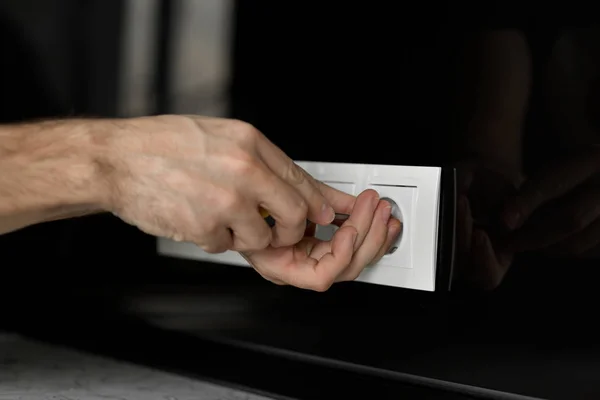 Close-up of an electrician\'s hand with a screwdriver disassembling a white electrical outlet on a black glass wall