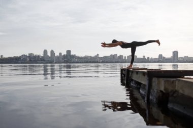 Genç kadın şehir arka plan ile sessiz ahşap iskelede Yoga egzersiz pratik. Spor ve eğlence şehir acele