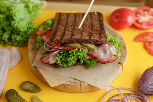 Juicy sandwich with grilled dark bread and bacon wait for you on wooden plate — Stock Photo, Image